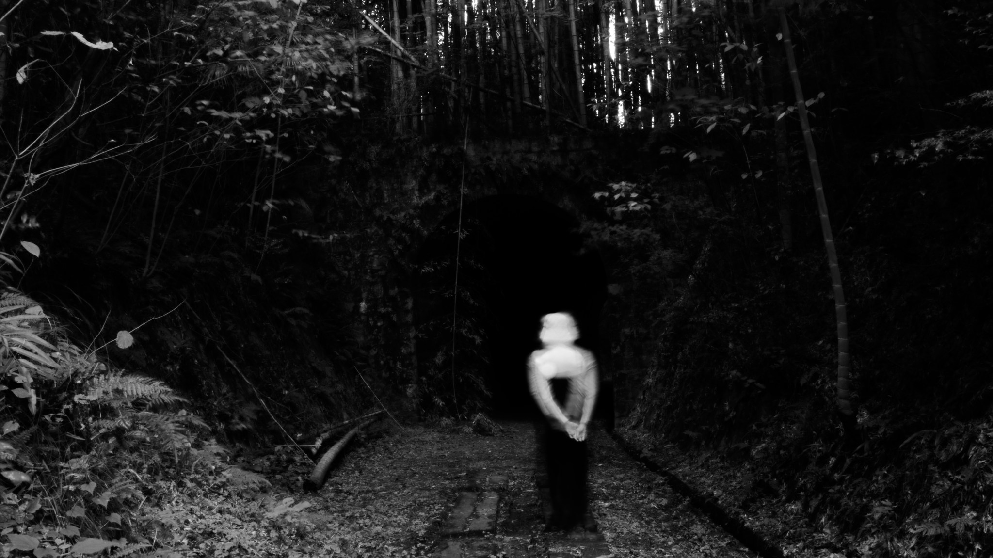 A blurred figure walks away from the camera toward a barely visible, pitch black arch in a hillside.
