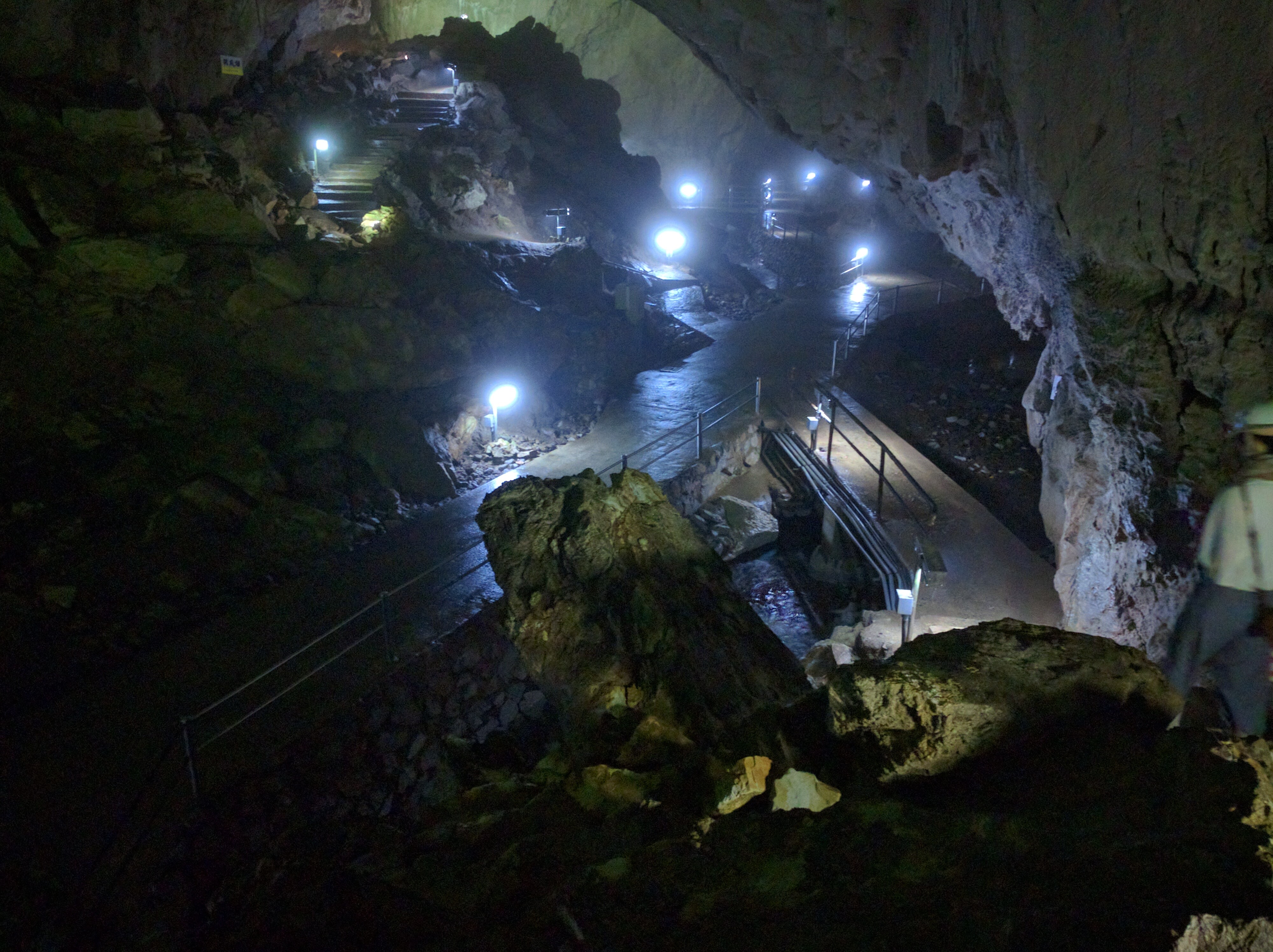 A picture taken from a raised area inside a cave, showing a winding concrete walkway lined with lights.