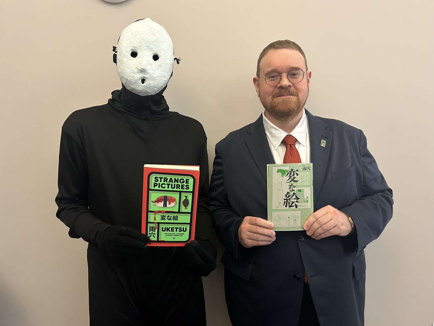 Jim and Uketsu standing next to each other, holding copies of Strange Pictures and Henna E.