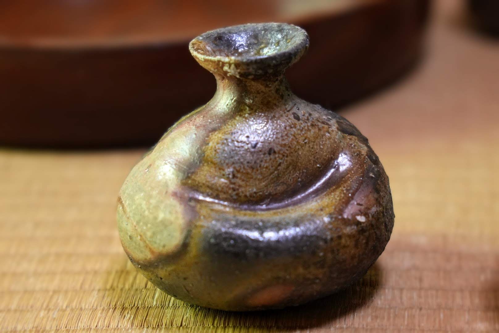 A small ceramic flask with a rounded shape and a sharp indentation along one side.