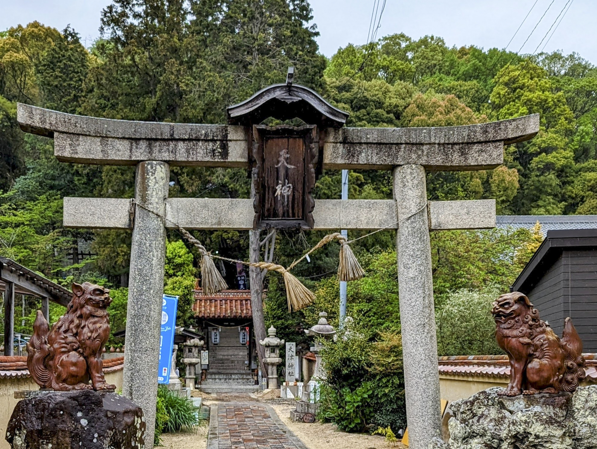 A concrete torii gate stands across a bricked path. To each side are reddish brown ceramic koma-inu dog statues.