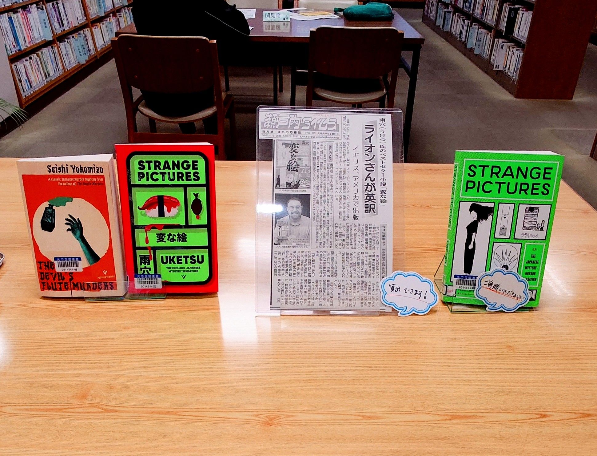 A tabletop display of The Devil's Flute Murders and the U. S. And U. K. Versions of Strange Pictures, along with a photocopy of a newspaper article about the translation of Strange Pictures.